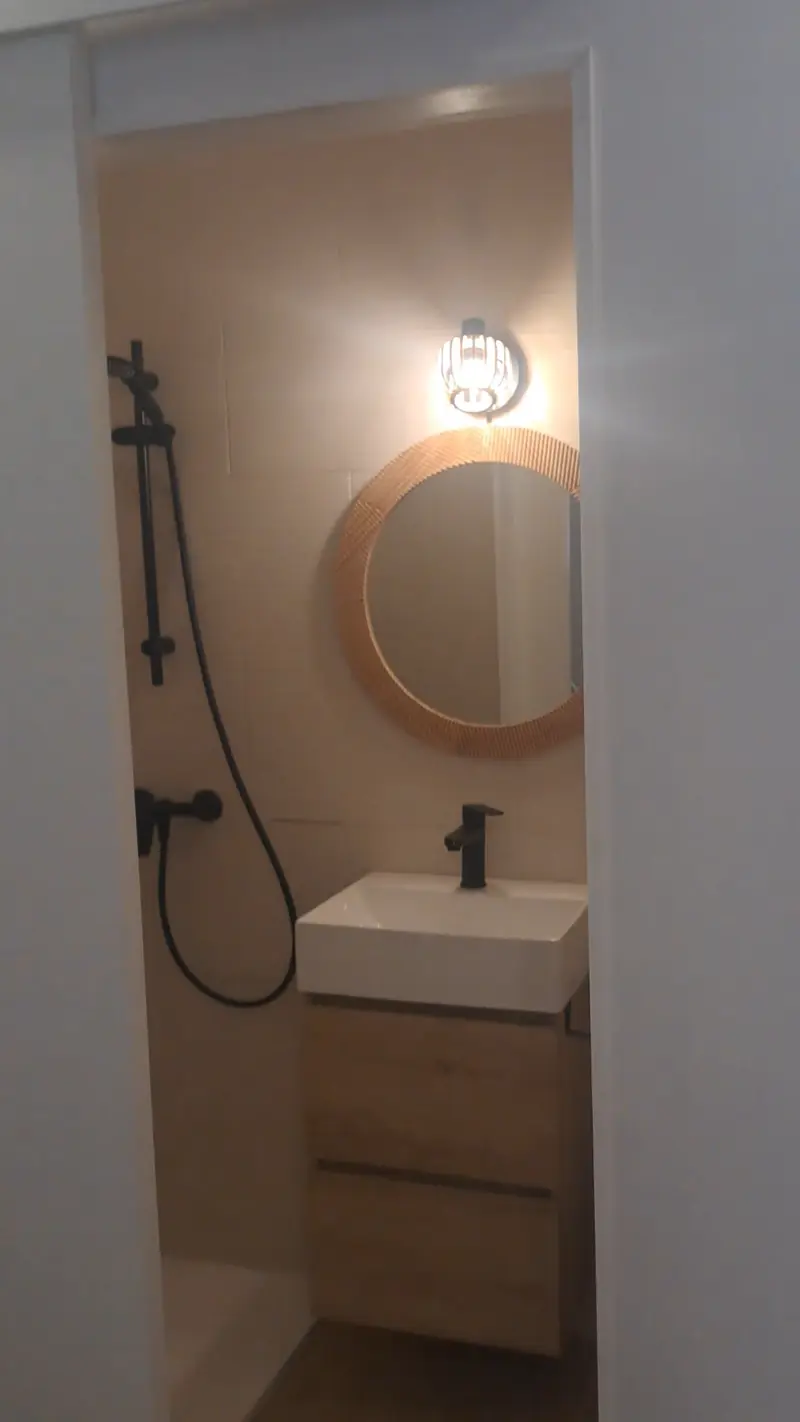 Baño reformado con lavabo de madera, espejo redondo y grifería negra