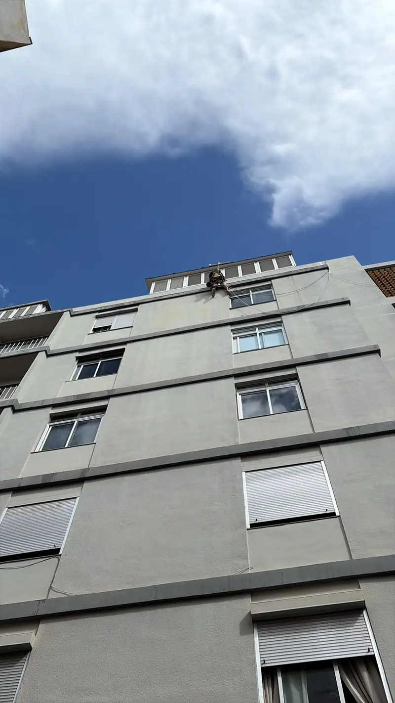 Edificio de cuatro plantas con un trabajador en la cornisa