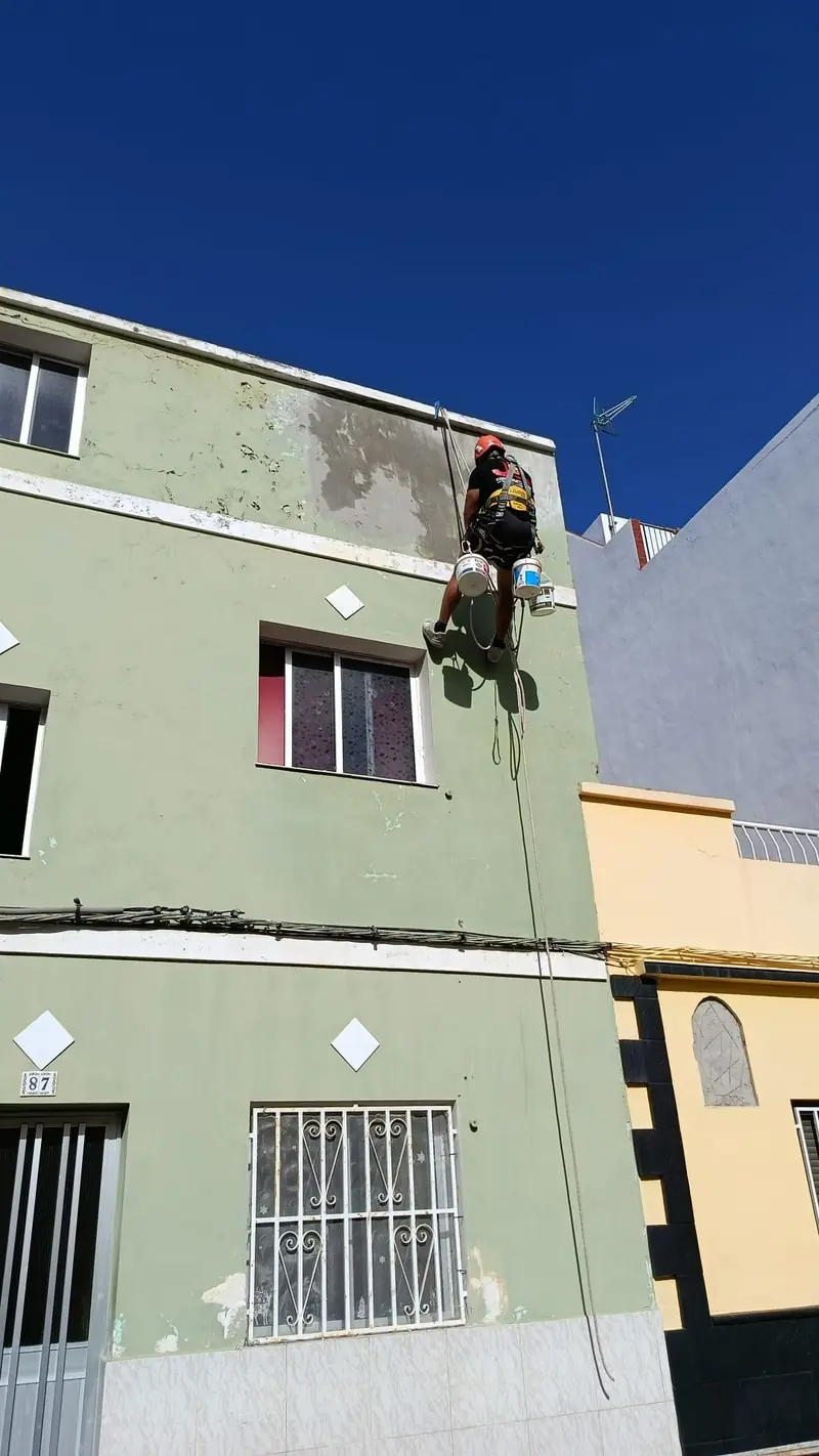 Trabajador colgado de cuerda pintando una fachada verde